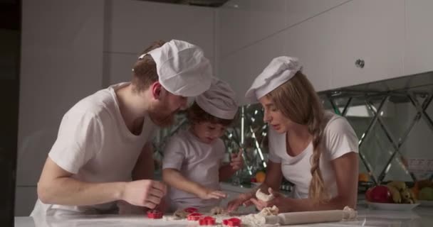笑顔の若い家族の肖像画は、キッチンで料理をしている。彼らは生地をこね、小麦粉でお互いの顔を磨く.白居心地の良いキッチンと穏やかな家族の雰囲気。4Kビデオ — ストック動画