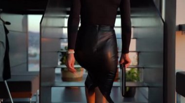 Siyah deri etekli bir bayan patronun arkadan görünüşü ofis merkezindeki merdivenlerden elinde bir klasörle çıkıyor.