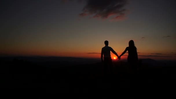 Ρομαντικό υπαίθριο πορτραίτο των δύο σιλουετών δίνοντας ο ένας στον άλλο τα χέρια, αγκαλιάζοντας και φιλώντας κατά τη διάρκεια του ηλιοβασιλέματος. Όμορφο τοπίο. Η γυναίκα κρατάει το μπουκέτο.. — Αρχείο Βίντεο