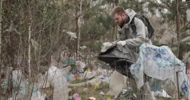 Lixo na floresta. Poluição do ambiente. Pessoas jogaram lixo ilegalmente na floresta. Lixo ilegal e desperdício na natureza. Problema ecológico em países não desenvolvidos. homem coleta lixo em — Vídeo de Stock