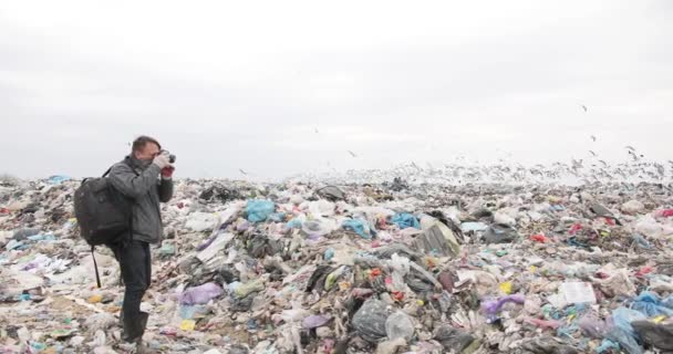 Male photographer with a large black backpack stands in a landfill and photographs an ecological disaster of people. ekology catastrophe. big peoples problem — Stock Video