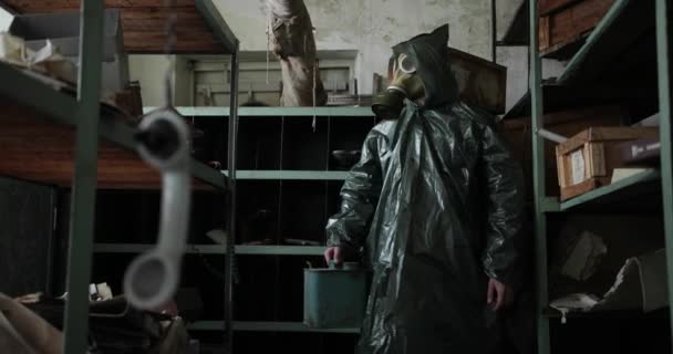 Gefahrenzone. Ein Mann in Spezialkleidung und Gasmaske steht mit einem Kanister in der Hand in einem zerstörten Raum. Mann in Regenmantel und Gasmaske. Technogene Katastrophe. virus COVID-19 — Stockvideo