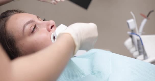 Jeune femme caucasienne assise sur une chaise dentaire au centre médical pendant que le médecin professionnel fixe les dents. Blanchiment des dents professionnel — Video