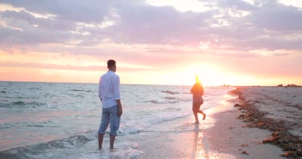 Schöne rosa Meer Sonnenuntergang. Ein Mann steht am Meer. Charmante Blondine mit langen Haaren läuft am Ufer entlang — Stockvideo