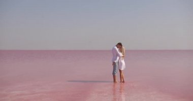 Pembe mineral gölünün arka planında duran mutlu romantik çift çöl gibi görünüyor. Ve bir adam gülümseyen sarışın bir kadına sarılıp onu öpüyor.
