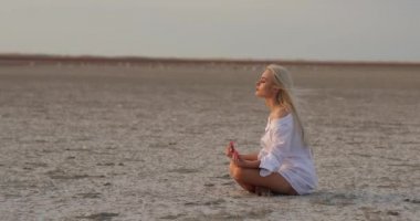 Kumda oturan çekici genç bir kadın. Meditasyon. Deniz kenarındaki Yogacı kadın güneş doğarken plajda kaygısız bir zen lotus yoga pozunda dinleniyor. Kadın meditasyonu