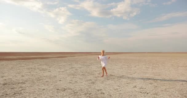 Egy vonzó szőke nő fut át a sztyeppén. fiatal nő fehér rövid ruha. — Stock videók