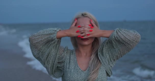 Красивая женщина покрывает лицо своими руками красивый яркий маникюр. Морской фон — стоковое видео