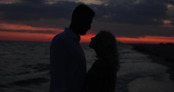 Una joven pareja mirándose con amor al atardecer, de cerca. Silueta de pareja besándose en sol rojo dorado y hermoso atardecer. Pareja joven y romántica — Vídeos de Stock