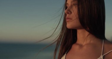 Huzurlu günbatımının tadını çıkaran güzel bir kadının portresi. Rüzgâr saçlara esiyor. 4K atış.