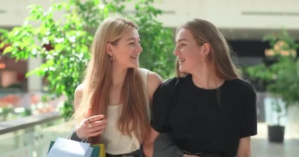 Deux jeunes belles femmes se promènent dans le centre commercial et regardent leurs achats. Des amis élégants marchent dans le centre commercial, rient et mènent une conversation passionnante. Vidéo 4K — Video