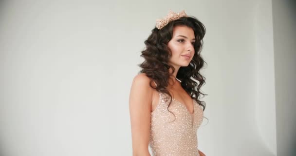 Model posing in the studio. Closeup of a woman in a golden crown looking straight in the camera while she poses in the white studio — Stock Video