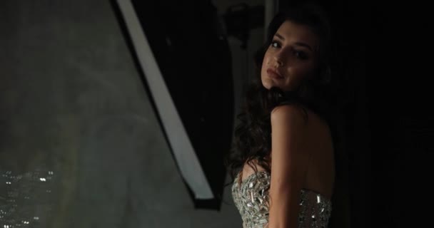Modèle posant en studio. Photo dramatique de jolie femme en robe étincelante posant derrière les lumières du studio dans l'obscurité — Video