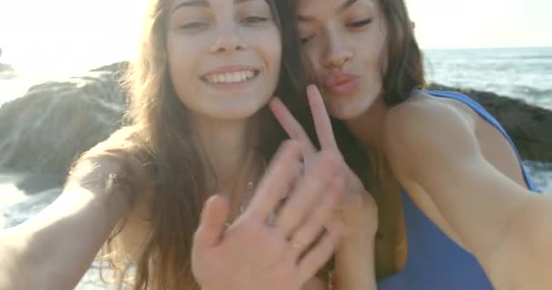 Duas belas jovens amigas felizes nas férias. Estão a tirar selfies na costa. A loira sedutora está beijando sua namorada na bochecha. — Vídeo de Stock