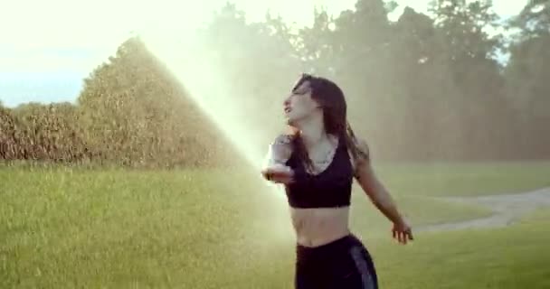 Emotioneel zonnig portret van de aantrekkelijke jonge brunette die plezier heeft terwijl ze danst en ronddraait in de regen vanuit de sproeier. — Stockvideo
