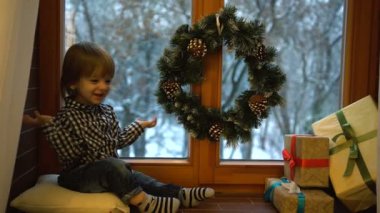 Pencerenin pervazında hediyelerle otururken sarı saçlı, gülen küçük çocuğun Noel portresi..