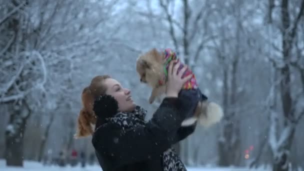 Happy beautiful ginger head woman is throwing her lovely fluffy pomeranian spitz into the air during the snowfall. — Stock Video