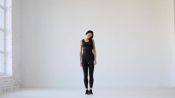 Vista de cuerpo entero. Deporte y Salud. La mujer en traje de gimnasio negro se calienta enrollando su cuello en una habitación blanca y aislada. — Vídeos de Stock