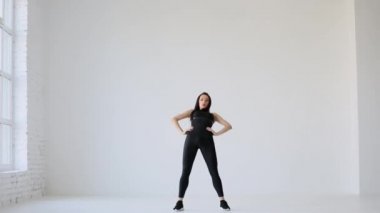 Siyah spor giyimli genç atletik kadın beyaz arka planda leğen kemiği daireleri çizerek ısınıyor. Spor eğitmenleri.