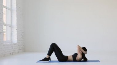 Siyah spor elbiseli esmer, beyaz izole odada egzersiz minderinin üzerinde mekik çekiyor..