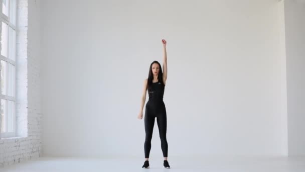 Sport tutorials. Lessons for beginners. The sportwoman is stretching her body by snatching her arms. She is raising them up at the white background. — Stock Video