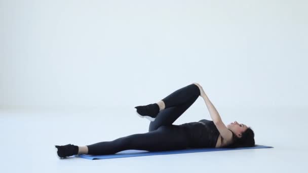 Молодая спортсменка-тренер разогревается, делая лежащие подколенные сухожилия на коврике для упражнений в студии. Учебники по фитнесу. Спорт для начинающих. — стоковое видео