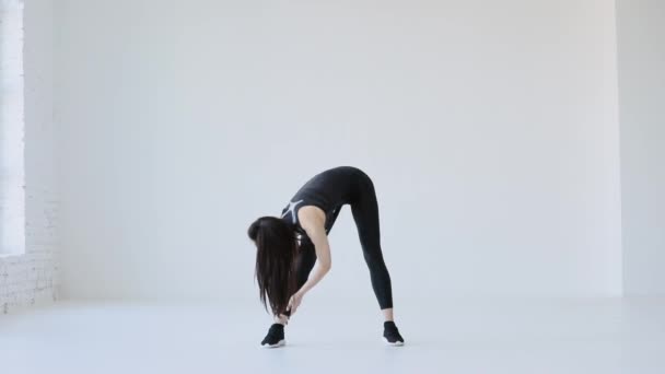 L'entraîneur sportif s'échauffe. Elle étire son corps en touchant ses jambes. L'emplacement du studio. Tutoriels Fitness et Pilates. — Video