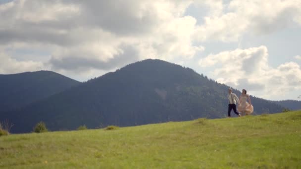 Чарівна старовинна вдягнена пара тримає руки, бігаючи по зеленому лугу на тлі гір. Красивий чоловік підбирає свого коханця і кружляє навколо . — стокове відео
