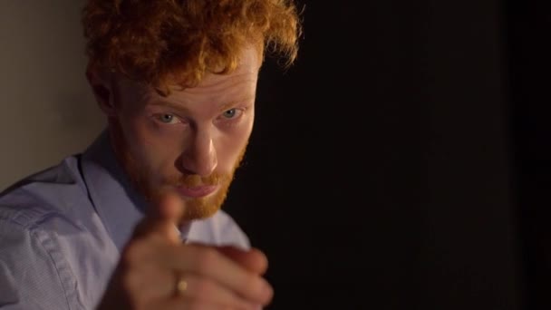 The pretty serious man with ginger hair and beard pointing with finger at camera and beckoning at the black background. — Stock Video