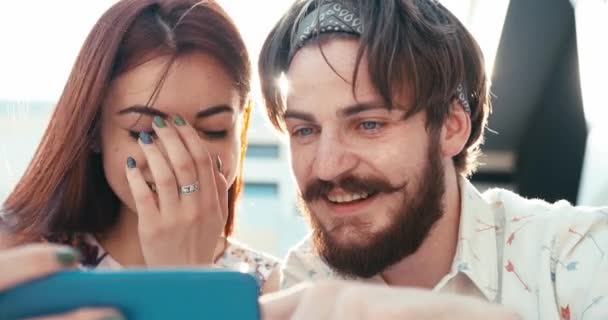 Portrait of the young couple of hipsters are laughing while watching vieo on the mobile phone. Flare light. 4k. — Stock Video