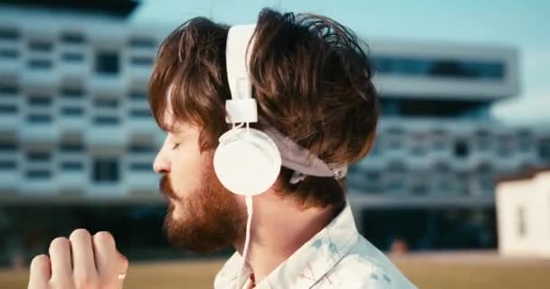 Porträt des jungen attraktiven männlichen Hipsters, der mit Kopfhörern tanzt und Musik genießt. 4k Filmmaterial. Draußen. — Stockvideo
