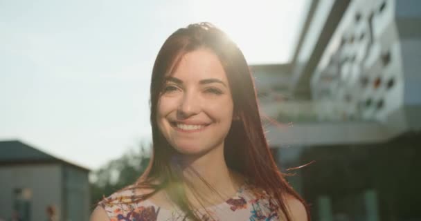 Retrato de la joven chica encantadora con el pelo rojo y bonita sonrisa mirando a la cámara en los soles. Mueve el pelo del viento. 4k. — Vídeo de stock