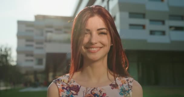 Positief prachtig meisje met rood haar en perfecte glimlach is op zoek naar de camera. Bewegend haar uit de wind. 4k. Close-up portret. — Stockvideo