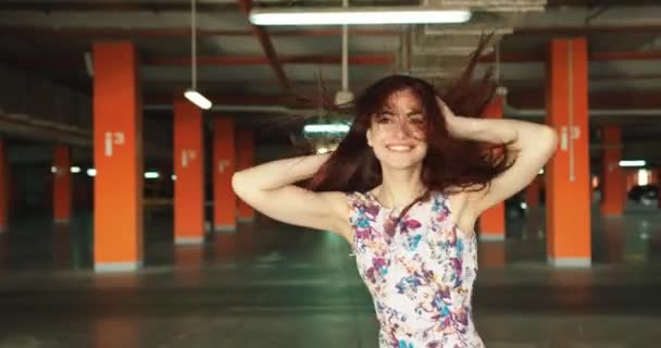 Belle brune positive avec un sourire charmant se promène et tourne dans le parking. Images 4k. — Video