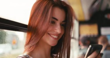 Güzel gülüşü olan, otobüste araba sürerken SMS okuyan çekici bir esmerin portresi. 4k.