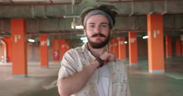 Un bel ragazzo hipster con la barba scura e la bandana nera sta ballando nel parcheggio. 4k filmati. — Video Stock