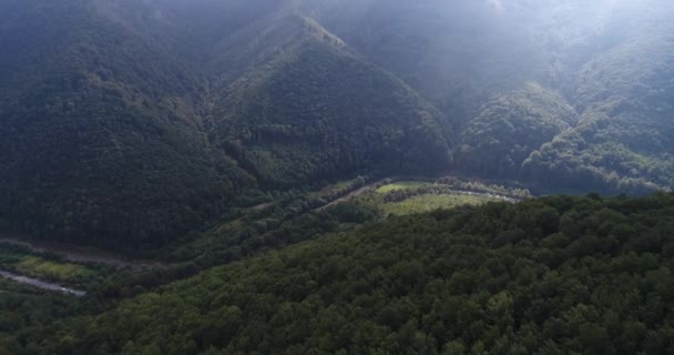 Volando helicóptero sobre las verdes montañas cubiertas de espeso bosque, río y carretera con coches de conducción. — Vídeos de Stock