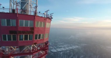 Şehrin arka planında, güzel gün batımında karla kaplı kırmızı radyo kulesinin etrafında dönen helikopter..