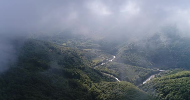 Vista de perto do helicóptero voador através de nuvens grossas sobre as belas montanhas ensolaradas cobertas com floresta verde e lago. — Vídeo de Stock