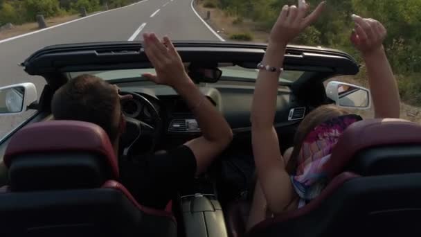 Back view of the loving couple having fun and raising hands up while driving in the cabriolet. — Stock Video