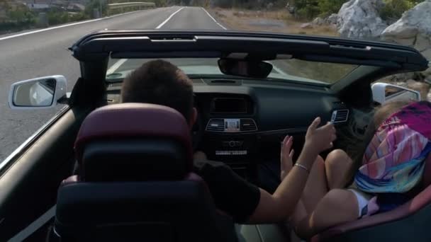 Back view of the couple raising hands up and holding while driving in the convertible along the road in the mountains. — Stock Video