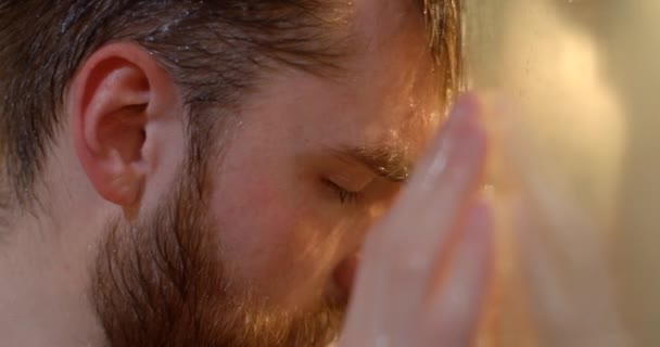 Detailní boční portrét nešťastného frustrovaného muže se zrzavým vousem a depresemi, který se smutně opírá o sklo ve sprše. — Stock video