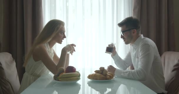 Reggelente a boldog, gyönyörű fiatal pár mosolyog, beszél és kávézik croissant-nal reggeli közben. — Stock videók