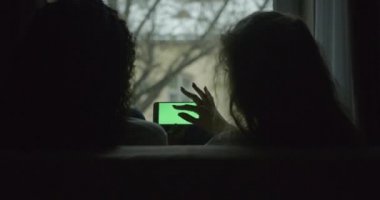 İki esmer ve sarışın kız arkadaşın, evdeki kanepede otururken cep telefonundan yeşil ekranlı bir şey izleyip konuştuklarını gördüm. Yüzü yok.