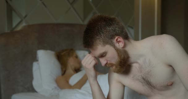 La coppia ha problemi a letto. L'uomo depresso testa di zenzero si preoccupa per lo sfondo sfocato della sua moglie delusa sdraiata a letto. — Video Stock