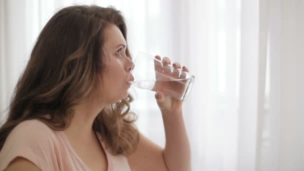 Молодая привлекательная женщина с избыточным весом пьет воду из стекла на диете. Боковой портрет. — стоковое видео