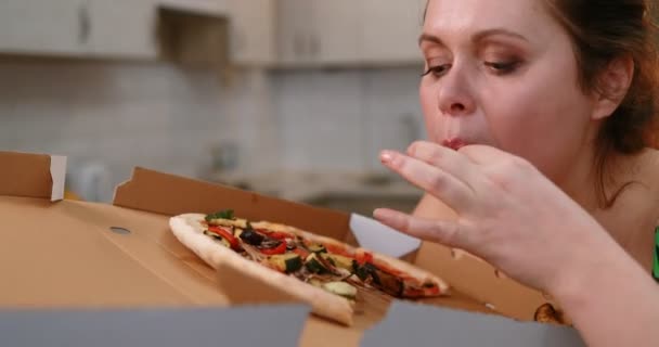 Portret van de zwaarlijvige vrouw die snel lekkere pizza eet in de keuken. — Stockvideo