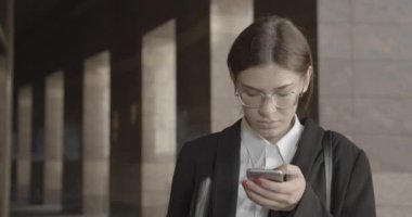 Ciddi bir iş kadınının portresi güzel gülüşlü cep telefonuyla sohbet ediyor. O, gözlük ve modern takım elbise takıyor. 4k.
