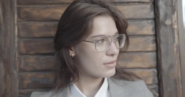 Ritratto dell'affascinante donna d'affari bruna con gli occhiali che sorride e guarda da parte su uno sfondo di legno. — Video Stock