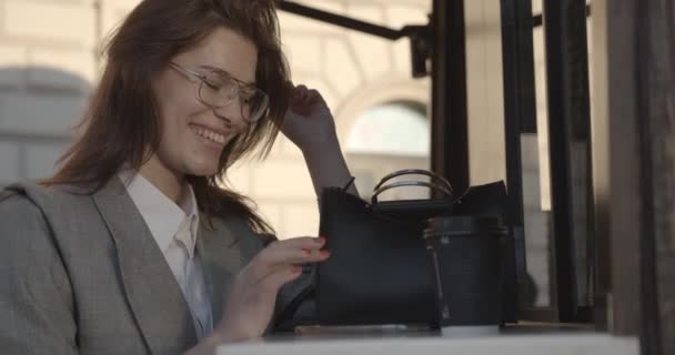 Atractiva mujer de negocios sonriente es chatear y navegar por el teléfono móvil mientras descansa en la cafetería. 4k. — Vídeo de stock